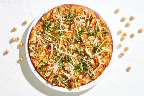 Chickpea pizza crust from California Pizza Kitchen on white plate. Chickpeas on white table surrounding pizza