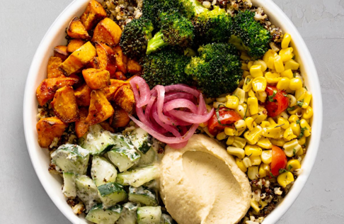 Power bowl with veggies and hummus in white bowl on white table